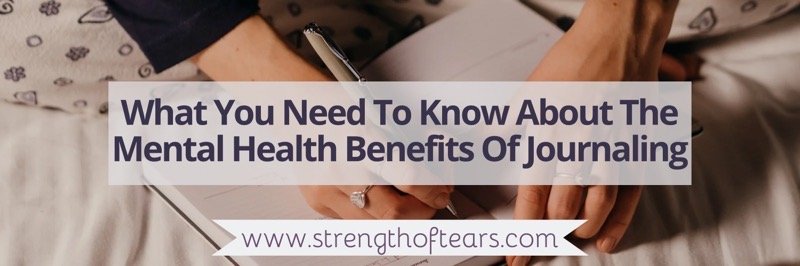 A white woman’s hands and black sleeves show her writing in a journal with a silver pen. The writing over the top says What You Need To Know About The Mental Health Benefits Of Journaling